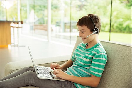 simsearch:6113-07790568,k - Boy wearing headset and using laptop on sofa Photographie de stock - Premium Libres de Droits, Code: 6113-07730552
