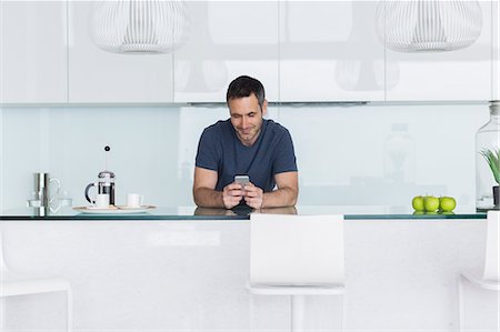 Man using cell phone in modern kitchen Foto de stock - Sin royalties Premium, Código: 6113-07730765