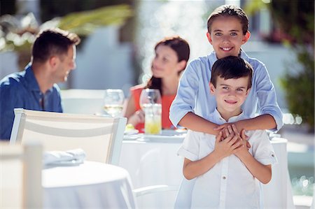 summer family meals - Portrait of smiling brother and sister, parents sitting at table in background Stock Photo - Premium Royalty-Free, Code: 6113-07808171