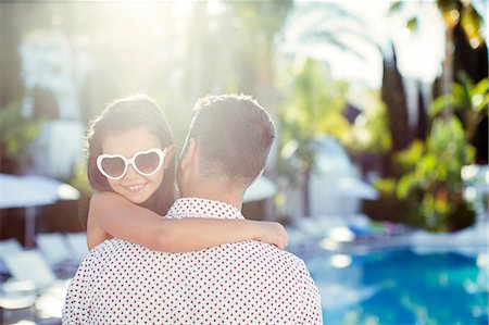Father carrying daughter wearing heart shaped sunglasses by swimming pool Photographie de stock - Premium Libres de Droits, Code: 6113-07808110