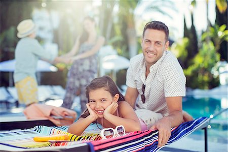 family walking outdoors not beach not hiking not water - Portrait of smiling father and daughter relaxing by swimming pool, mother and daughter in background Stock Photo - Premium Royalty-Free, Code: 6113-07808130