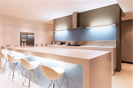 simsearch:6113-07808254,k - Modern white kitchen with kitchen island and stools illuminated at night Stock Photo - Premium Royalty-Free, Code: 6113-07808291