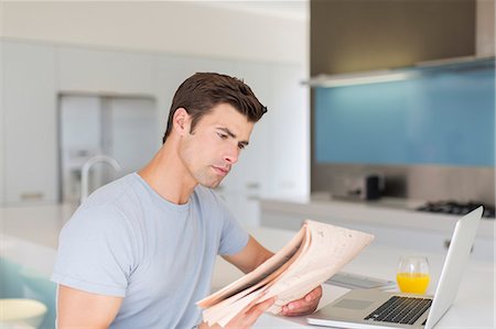 simsearch:6108-05875070,k - Man reading newspaper in modern kitchen, laptop and orange juice on counter Stock Photo - Premium Royalty-Free, Code: 6113-07808233