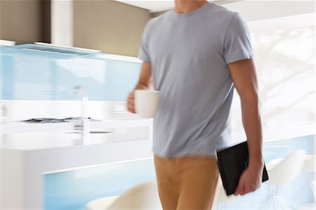 Man carrying coffee cup and digital tablet walking through modern kitchen Photographie de stock - Premium Libres de Droits, Code: 6113-07808236