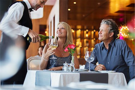 simsearch:6113-07808638,k - Mature couple sitting at restaurant table, waiter pouring white wine into woman's glass Foto de stock - Sin royalties Premium, Código: 6113-07808560