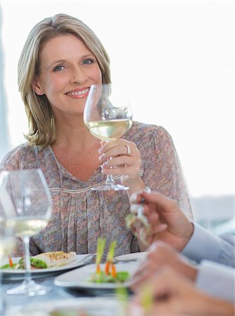 Portrait of smiling woman holding glass of white wine at restaurant table Stock Photo - Premium Royalty-Free, Code: 6113-07808575