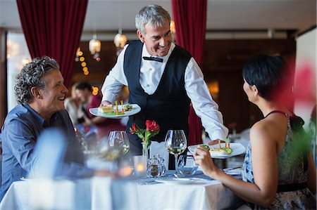 simsearch:6113-07808638,k - Smiling waiter serving fancy dishes to mature couple sitting at table in restaurant Foto de stock - Sin royalties Premium, Código: 6113-07808642