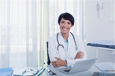 Portrait of smiling female doctor sitting with arms crossed at desk with laptop Photographie de stock - Premium Libres de Droits, Code: 6113-07808657