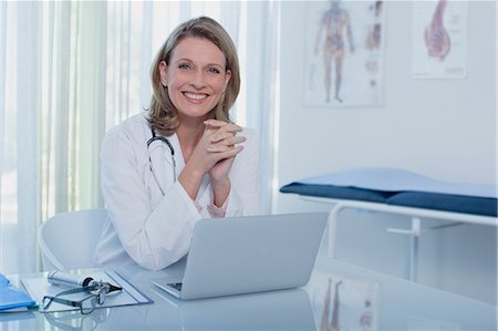 Portrait of smiling female doctor sitting at desk with laptop Photographie de stock - Premium Libres de Droits, Code: 6113-07808659