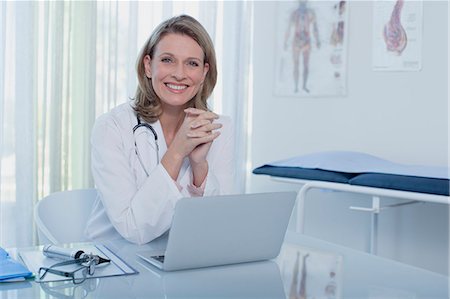 simsearch:6113-07905909,k - Portrait of smiling female doctor sitting at desk with laptop in office Stock Photo - Premium Royalty-Free, Code: 6113-07808679