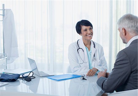 photos of doctors with patients - Smiling female doctor talking to patient at desk in office Stock Photo - Premium Royalty-Free, Code: 6113-07808682