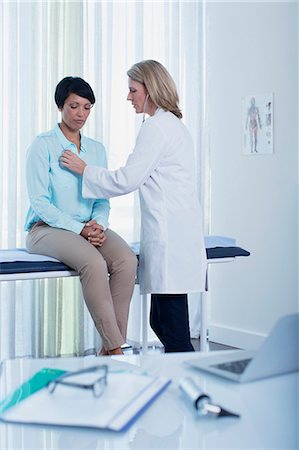 Female doctor examining her patient in office, laptop, otoscope, file and glasses on desk in foreground Photographie de stock - Premium Libres de Droits, Code: 6113-07808708