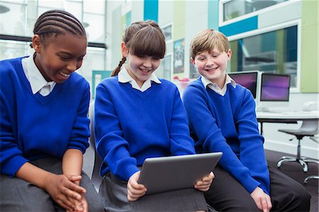 simsearch:6113-07961519,k - Primary school children wearing blue school uniforms holding digital tablet and smiling in classroom Fotografie stock - Premium Royalty-Free, Codice: 6113-07961494