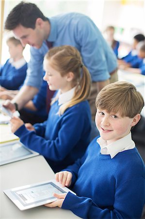 Portrait of schoolboy sitting with digital tablet in classroom, children and teacher in background Stock Photo - Premium Royalty-Free, Code: 6113-07961438