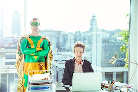 Superhero standing near businesswoman working in office Stock Photo - Premium Royalty-Free, Code: 6113-07961674