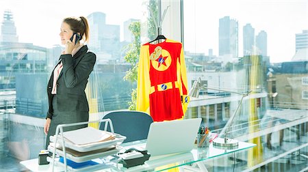 superhero business - Businesswoman talking on cell phone with superhero costume behind her Foto de stock - Sin royalties Premium, Código: 6113-07961742
