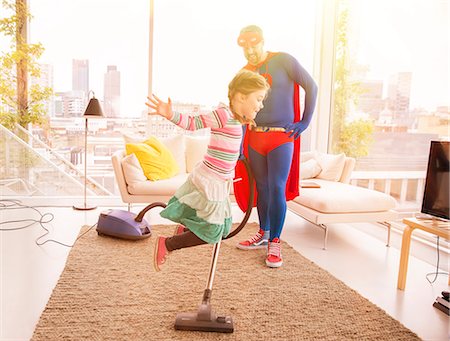 Superhero father vacuuming while daughter jumps in living room Stock Photo - Premium Royalty-Free, Code: 6113-07961733