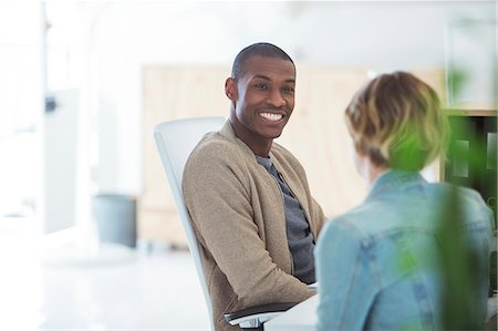 Man and woman sitting in office,smiling and talking Stock Photo - Premium Royalty-Free, Code: 6113-07991863