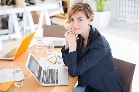 portrait woman short hair - Portrait of woman sitting at desk with laptop in office Stock Photo - Premium Royalty-Free, Code: 6113-07991875