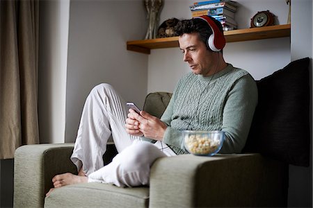 Man sitting in armchair with headphones using smartphone Stock Photo - Premium Royalty-Free, Code: 6113-07991835