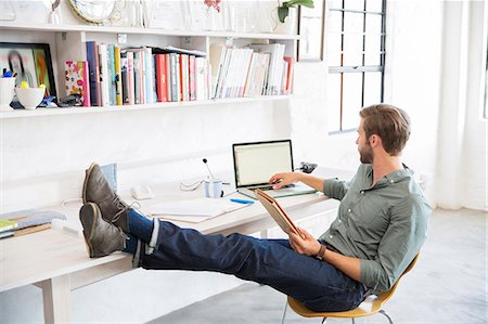 person sitting at desk picture - Portrait of young man sitting with legs on desk working with laptop Stock Photo - Premium Royalty-Free, Code: 6113-07992060