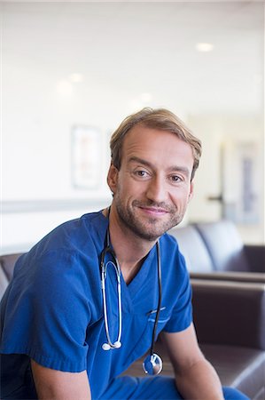 Portrait of mid adult doctor smiling and sitting on leather sofa in hospital corridor Stock Photo - Premium Royalty-Free, Code: 6113-07905855