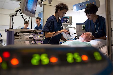 simsearch:6113-07905962,k - Doctors attending patient in intensive care unit, monitoring equipment in foreground Stock Photo - Premium Royalty-Free, Code: 6113-07905964