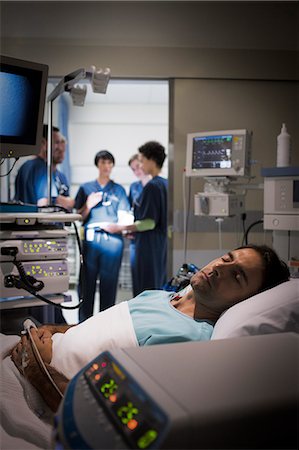 simsearch:6113-07905964,k - Patient lying in bed in intensive care unit, doctors discussing in background Photographie de stock - Premium Libres de Droits, Code: 6113-07905966