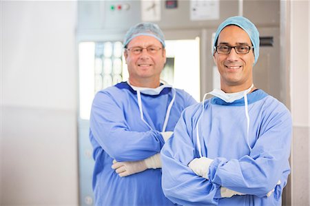 Two smiling doctors with arms crossed, wearing surgical clothing and eyeglasses in hospital Photographie de stock - Premium Libres de Droits, Code: 6113-07905990