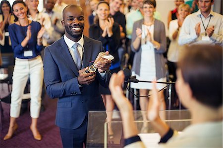 Portrait of young man holding trophy, standing in conference room, smiling to applauding audience Foto de stock - Sin royalties Premium, Código: 6113-07906084