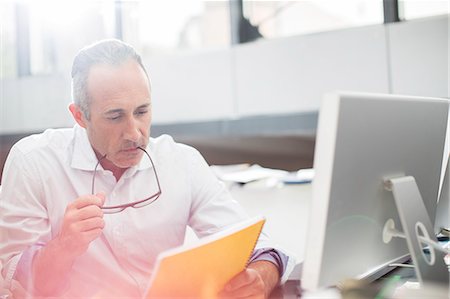 simsearch:6113-07906197,k - Businessman reading paperwork at office desk Stock Photo - Premium Royalty-Free, Code: 6113-07906143