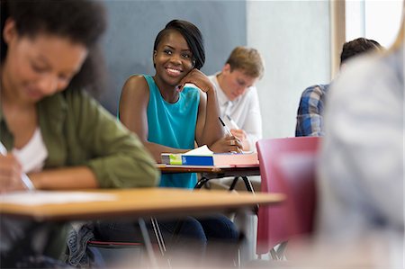 simsearch:6113-07808769,k - Smiling university student sitting at desk with hand on chin Foto de stock - Sin royalties Premium, Código: 6113-07906473