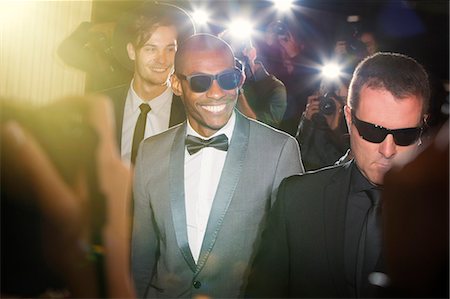 Smiling celebrity in sunglasses being photographed by paparazzi photographers at event Photographie de stock - Premium Libres de Droits, Code: 6113-08088244