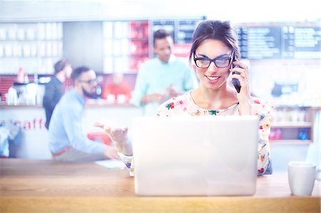 simsearch:6113-07159245,k - Businesswoman using laptop and talking on cell phone in cafe Stock Photo - Premium Royalty-Free, Code: 6113-08088510