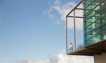 Men standing on balcony of glass bump out against blue sky Stock Photo - Premium Royalty-Free, Code: 6113-08171249