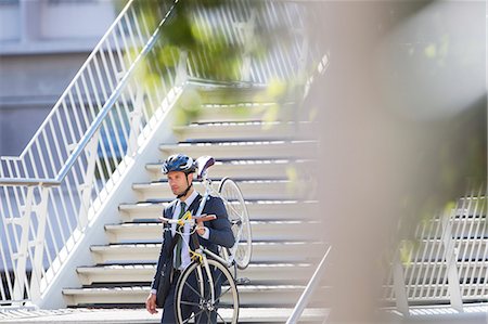 Businessman in suit and helmet carrying bicycle down urban stairs Foto de stock - Sin royalties Premium, Código: 6113-08171262