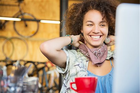 Smiling woman at laptop in bike shop adjusting neck scarf Stock Photo - Premium Royalty-Free, Code: 6113-08171281