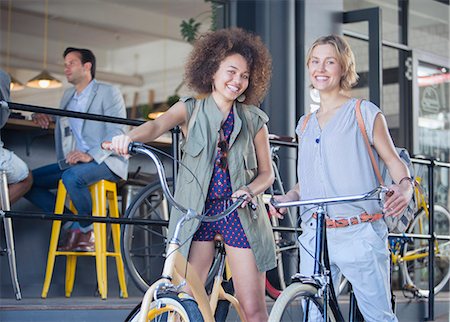 simsearch:6113-08171306,k - Portrait smiling women on bicycles outside cafe Fotografie stock - Premium Royalty-Free, Codice: 6113-08171282