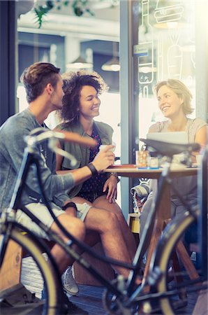 Friends hanging out at cafe table behind bicycle Stock Photo - Premium Royalty-Free, Code: 6113-08171292