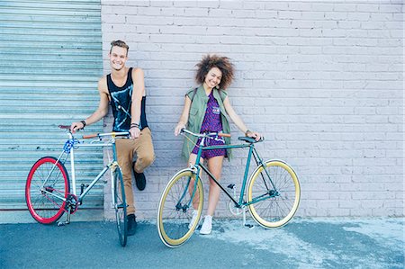 Portrait young man and young woman with bicycles at urban wall Stock Photo - Premium Royalty-Free, Code: 6113-08171296