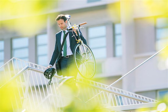 Businessman in suit carrying bicycle in city Stock Photo - Premium Royalty-Free, Image code: 6113-08171298