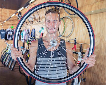 simsearch:6113-08171368,k - Portrait smiling young man holding bicycle wheel in bicycle shop Foto de stock - Royalty Free Premium, Número: 6113-08171353