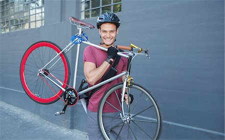 Portrait smiling young man carrying bicycle on urban sidewalk Stock Photo - Premium Royalty-Free, Code: 6113-08171362