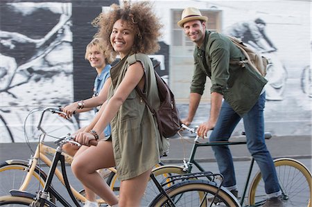 simsearch:6113-08171306,k - Portrait smiling friends riding bicycles on urban street Fotografie stock - Premium Royalty-Free, Codice: 6113-08171365