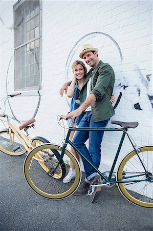 simsearch:6113-08171317,k - Portrait smiling couple with bicycles hugging at urban wall Stock Photo - Premium Royalty-Free, Code: 6113-08171370