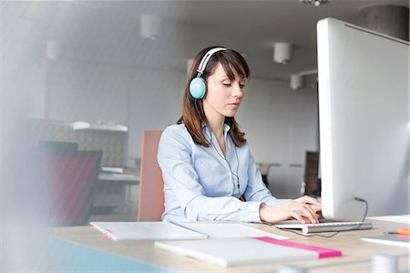 Brunette businesswoman with headphones working at computer in office Stock Photo - Premium Royalty-Free, Code: 6113-08171455