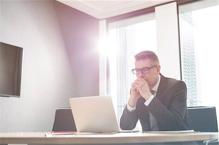 simsearch:6113-07542425,k - Focused businessman working at laptop in sunny office Stock Photo - Premium Royalty-Free, Code: 6113-08171420