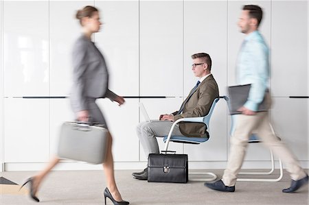 Businessman working at laptop in lobby behind business people on the move Stock Photo - Premium Royalty-Free, Code: 6113-08171428