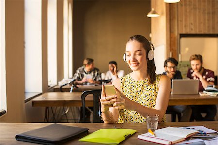 Casual businesswoman with headphones using cell phone in office Stock Photo - Premium Royalty-Free, Code: 6113-08105377