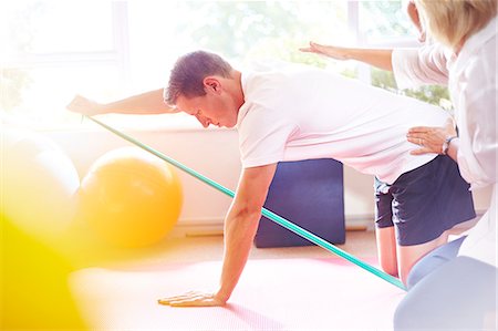 Physical therapist guiding man pulling resistance band Foto de stock - Sin royalties Premium, Código: 6113-08105479